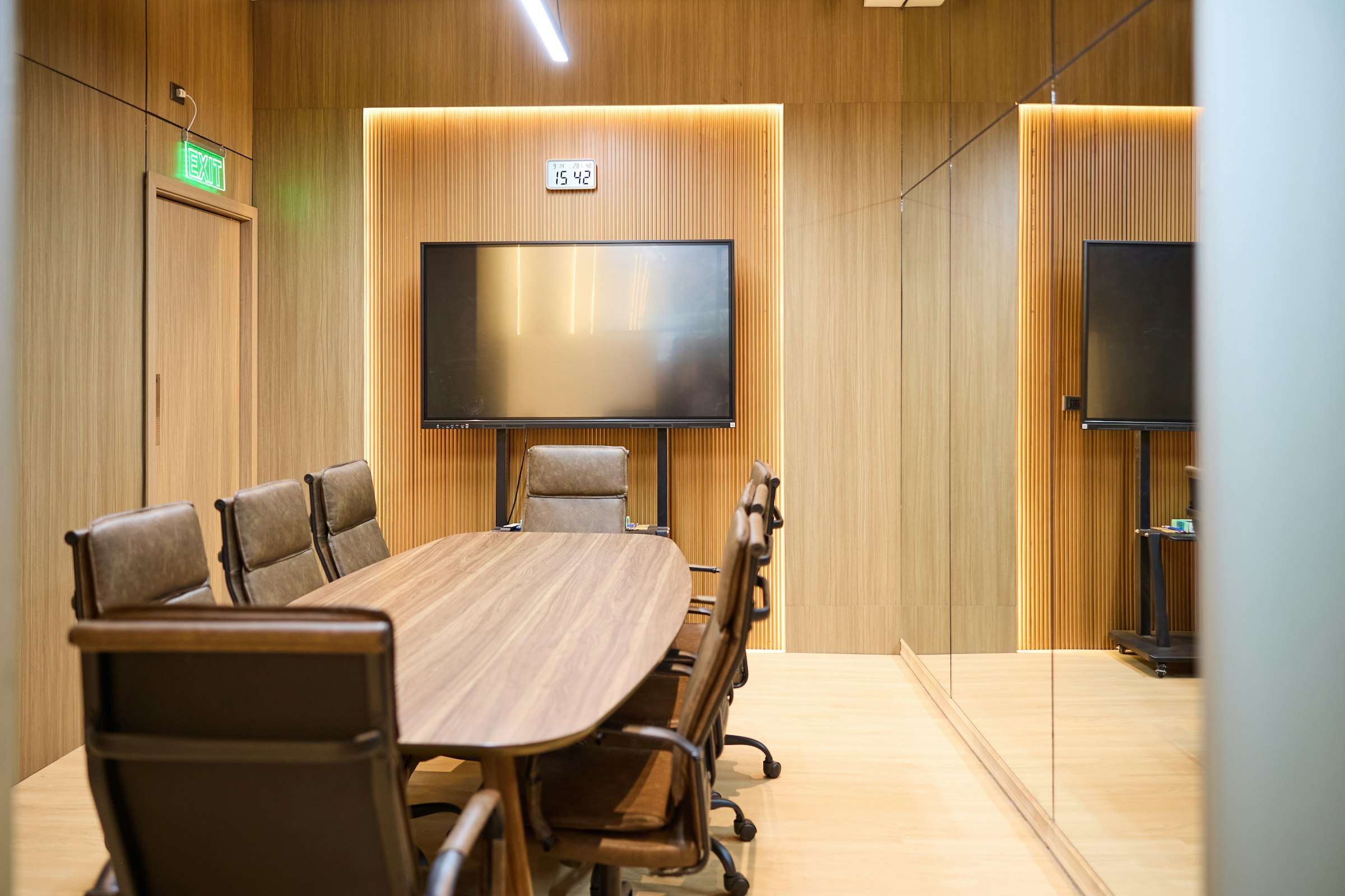 Voorbeeldfoto: een directiekamer met een groot scherm op een standaard, leren stoelen en een verlichte houten wand.